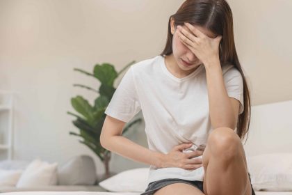 a woman sitting on the bed holding her stomach and head