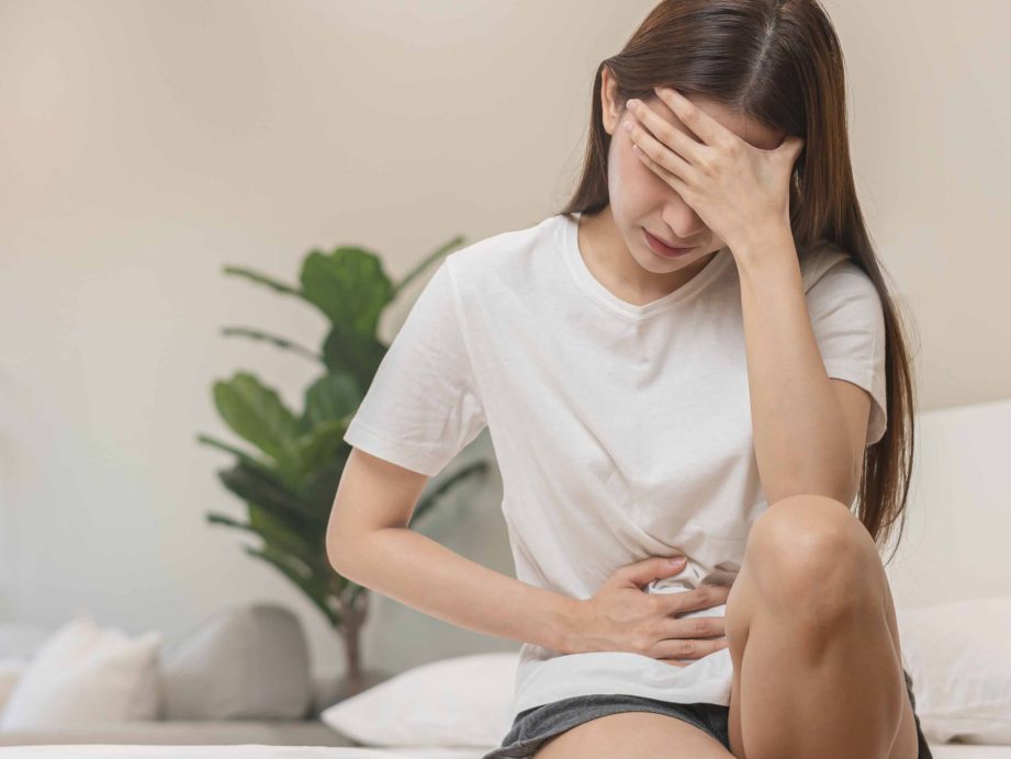 a woman sitting on the bed holding her stomach and head