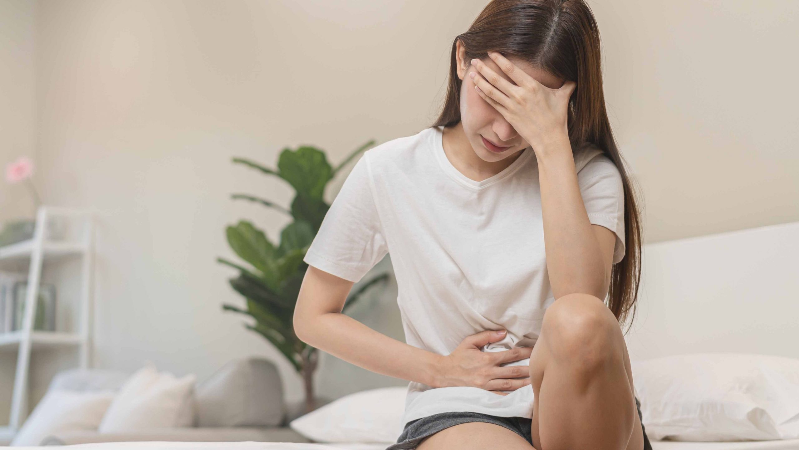 a woman sitting on the bed holding her stomach and head