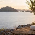 A round meditation cushion on a woven mat overlooking the sea at sunset in Greece
