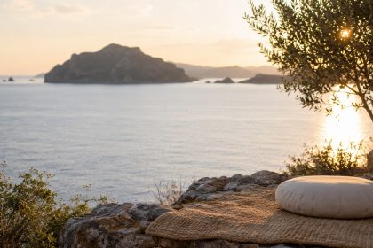 A round meditation cushion on a woven mat overlooking the sea at sunset in Greece