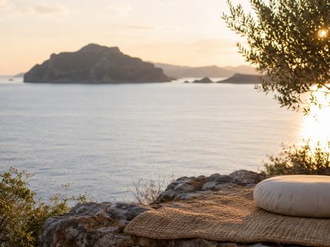A round meditation cushion on a woven mat overlooking the sea at sunset in Greece