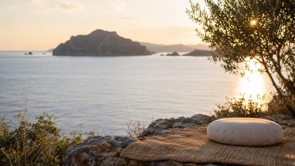 A round meditation cushion on a woven mat overlooking the sea at sunset in Greece